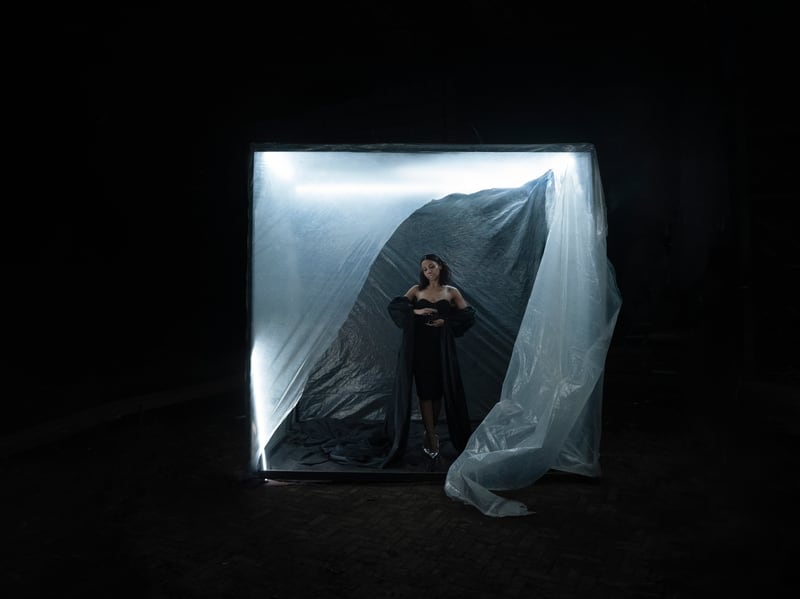 A lit cube of plastic sheeting standing in a black room, a figure inside it