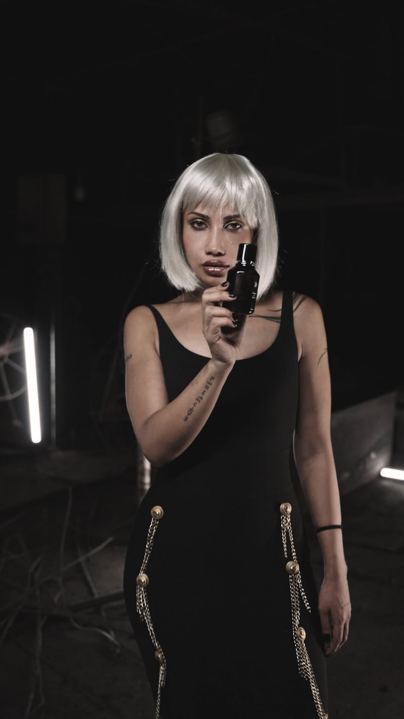 A woman in a white bob wig with the First + Cut flacon, a still from the film