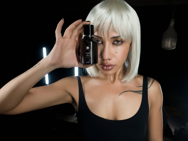 A woman in a white bob wig holding the First + Cut flacon beside her eye, the label fully legible