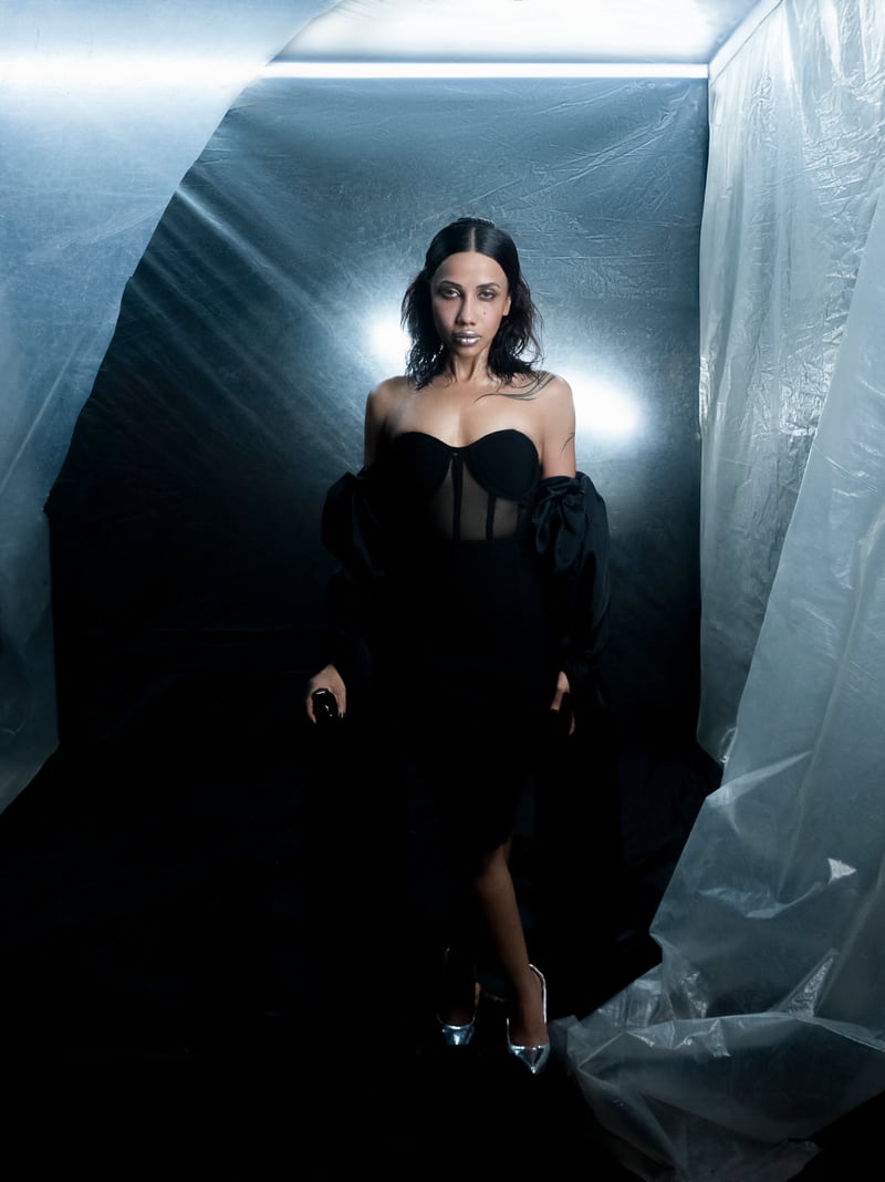A figure standing inside a lit cube of plastic sheeting in a black room