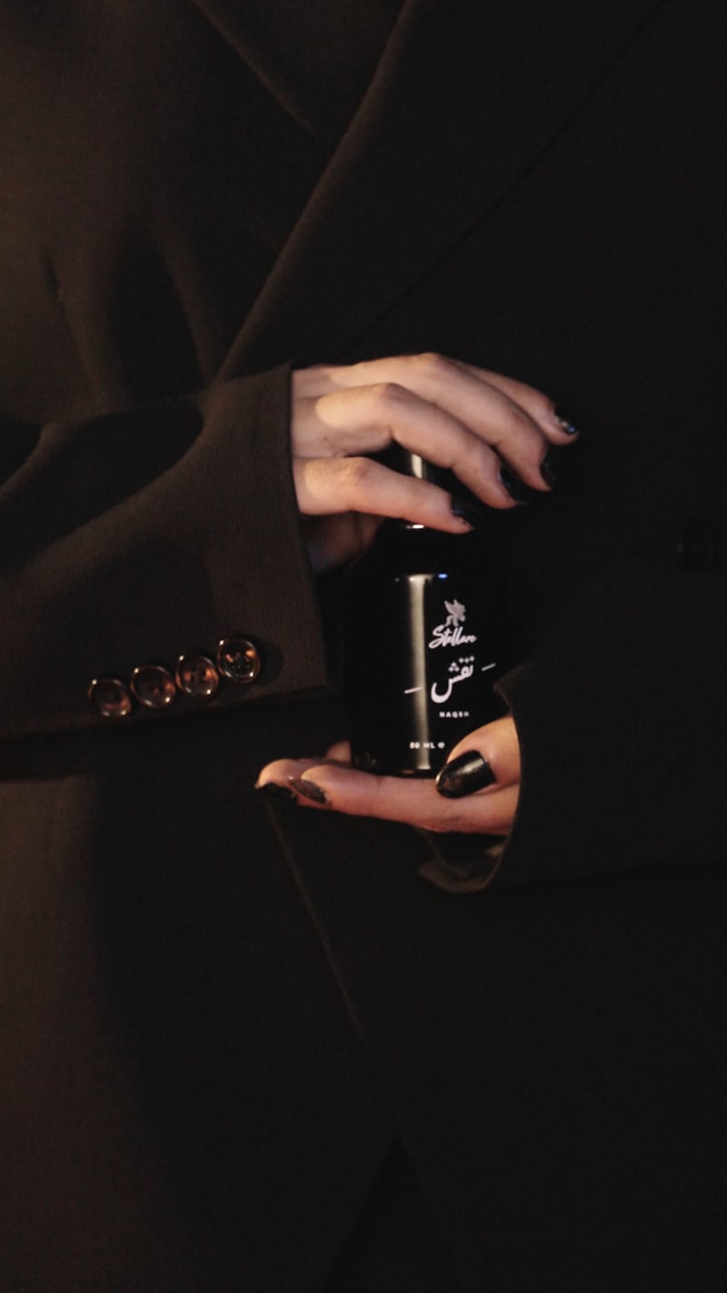 The Naqsh flacon held against a black coat, the label legible