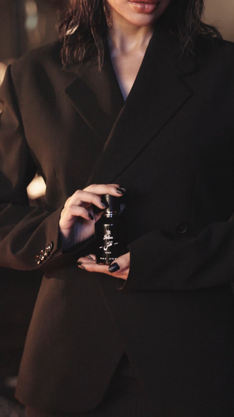 The Naqsh flacon in a hand at the waist of a black coat
