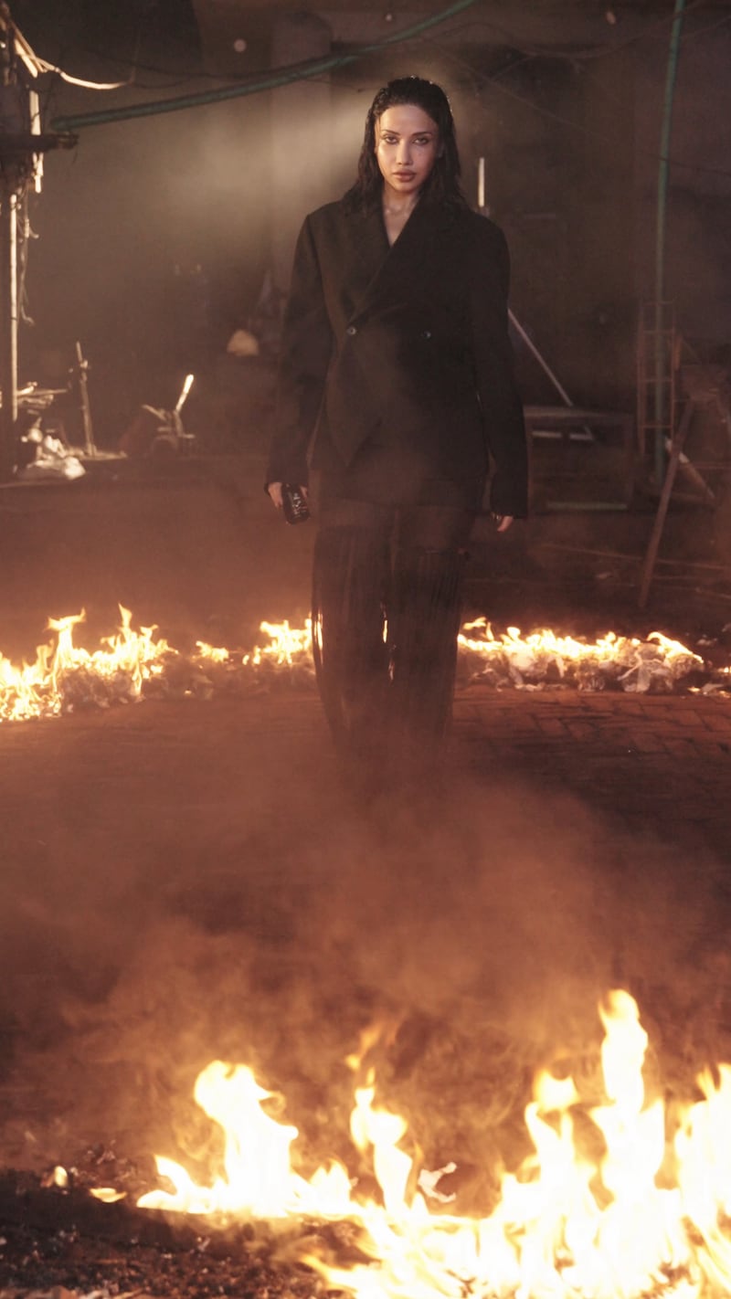 A figure standing inside a ring of fire in a smoke filled warehouse