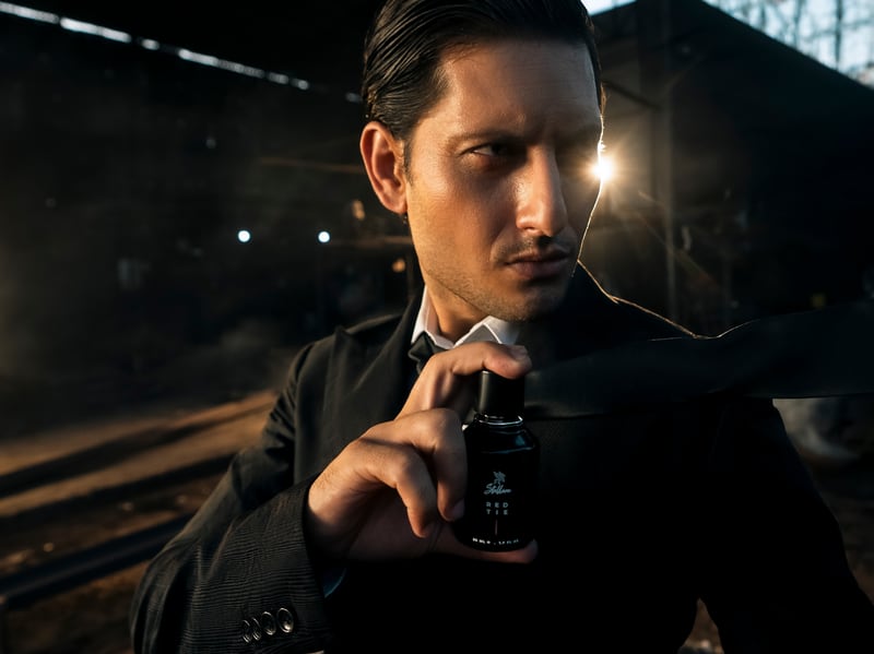 A man in a dark suit on a factory floor holding the Red Tie flacon at his chest, direct to camera